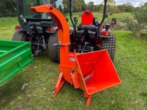Roter Anbau-Holzhäcksler zwischen zwei kleinen Traktoren auf einer Wiese